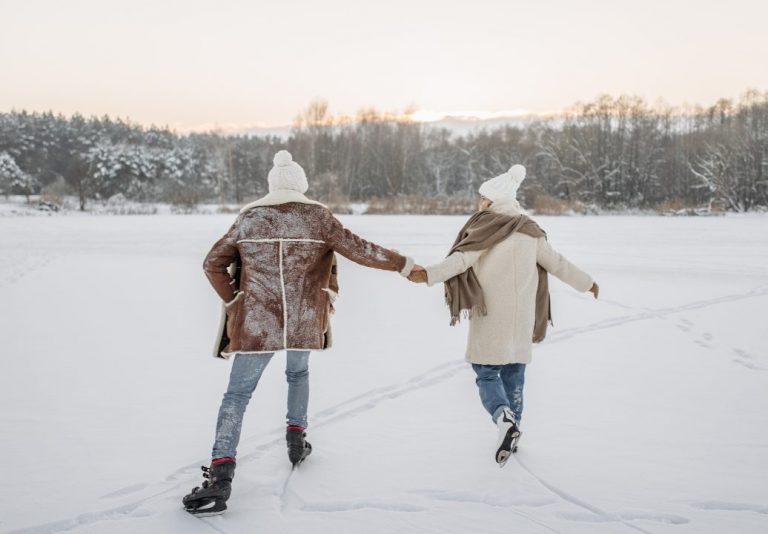 Deux personnes en patins sur un lac gelé et enneigé, bordé d’une forêt givrée