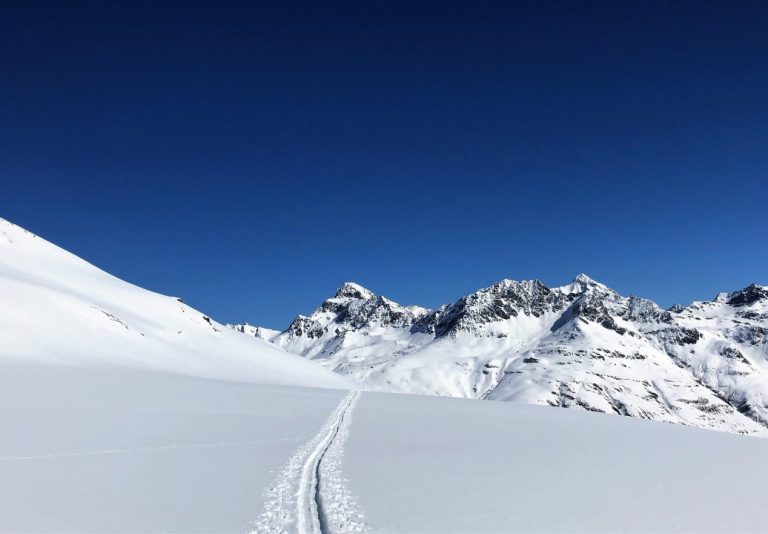 Trace de ski dans la neige fraîche, au pied d’une crête enneigée sous un ciel bleu