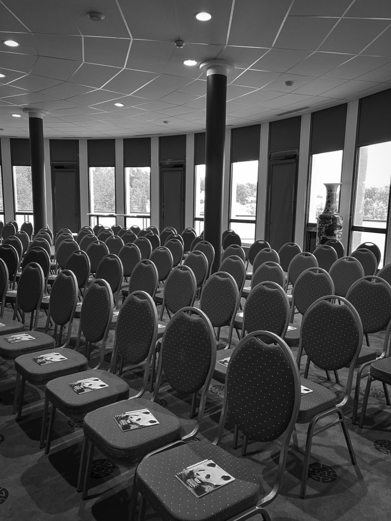 Salle de plénière prête pour le séminaire d’un groupe bancaire au Zoo de Beauval, des carnets posés sur les chaises, en noir et blanc