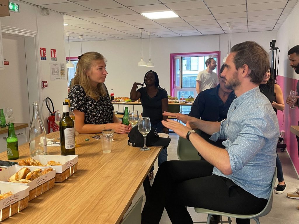 Deux invités de l’afterwork Ouicar en pleine conversation autour d’une table en bois garnie de pain et de boissons, soirée organisée par Weevup