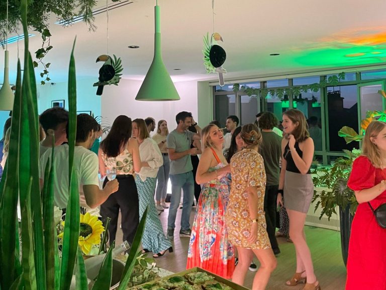 Collaborateurs de Havea Group en tenues d’été discutant sous des suspensions vertes, des toucans décoratifs et des plantes, pendant la summer party organisée par Weevup dans leurs locaux parisiens