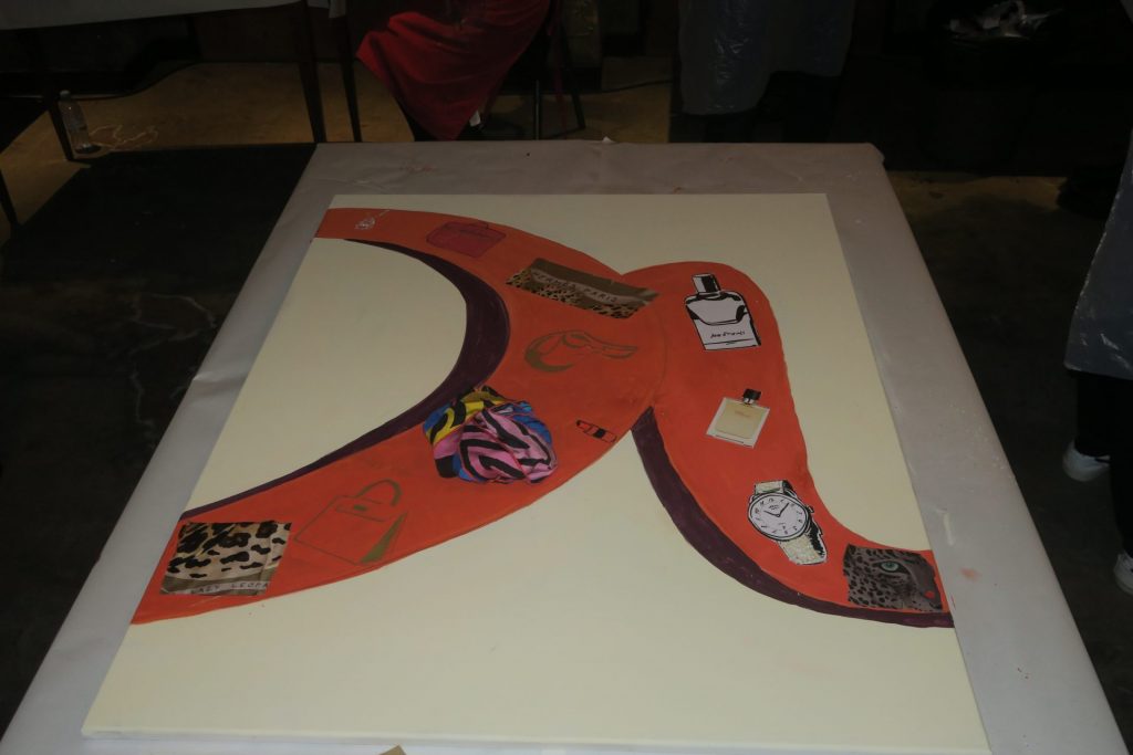Grande toile peinte en orange et ornée de collages, posée sur une table pendant l’événement Hermès au Kube Hôtel, organisé par Weevup