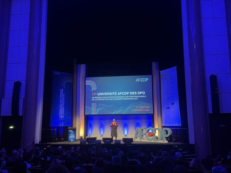 Intervenante sur scène devant le grand écran et les lettres AFCDP en volume, face au public de la convention annuelle à la Maison de la Chimie