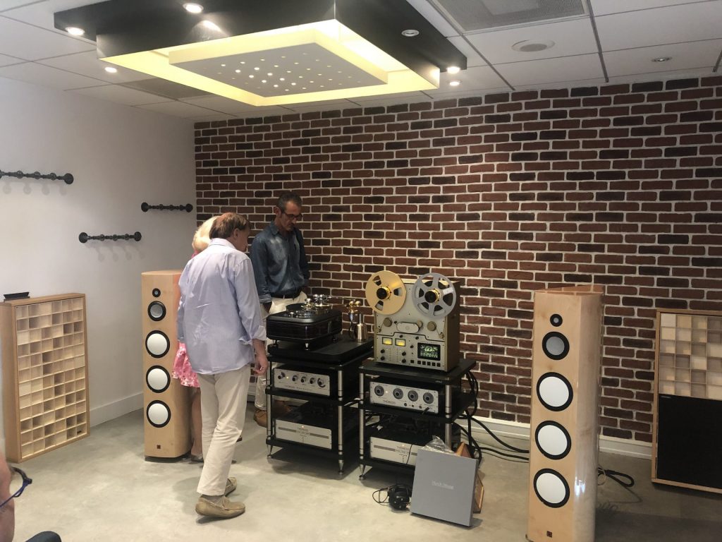Visiteurs devant des enceintes colonnes et un magnétophone à bandes dans un showroom du salon Publison, coordonné par Weevup