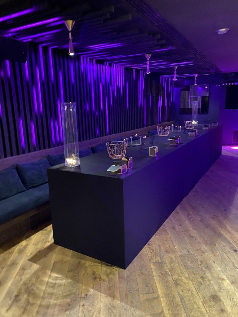 Long comptoir noir et banquettes sous un éclairage violet, dans la salle de la soirée cocktail Scalian organisée par Weevup à Paris
