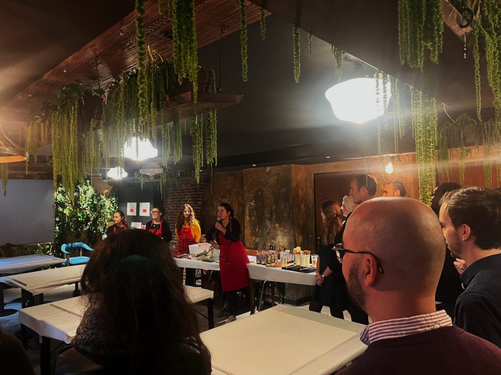 Participants rassemblés autour de grandes tables blanches au Kube Hôtel, face à une intervenante en tablier rouge, pendant l’événement Hermès organisé par Weevup