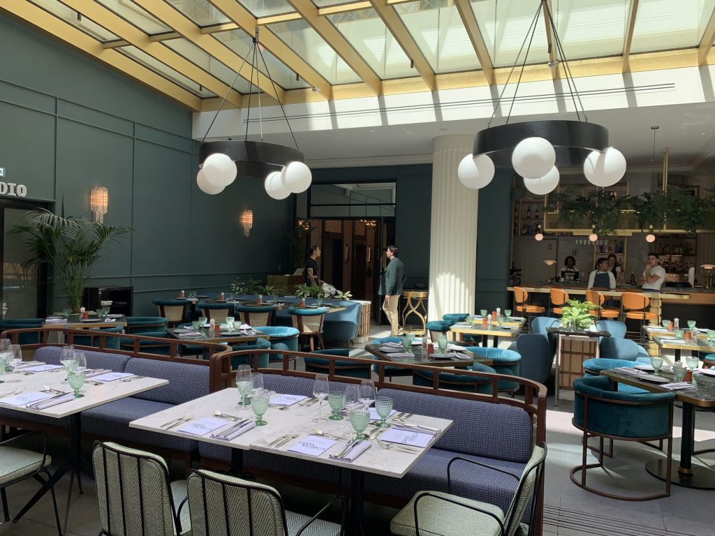Salle sous verrière avec banquettes bleues et tables dressées, à l’hôtel Kimpton, pour la soirée team building organisée par Weevup