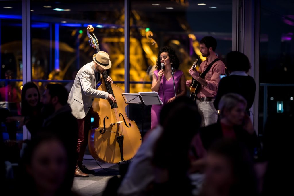 Trio de musiciens, contrebasse, chant et guitare, devant une baie vitrée de nuit pendant le séminaire international SVR organisé par Weevup à Paris