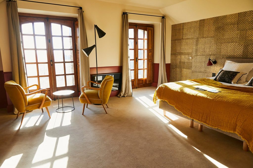 Chambre lumineuse avec lit, fauteuils jaunes et portes-fenêtres, dans le château du séminaire résidentiel du CODIR de Dior organisé par Weevup