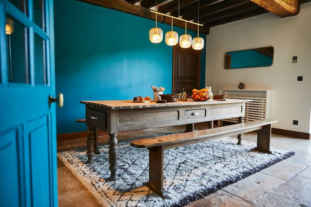 Salle à manger aux murs bleus avec grande table en bois et banc, dans le château choisi par Weevup pour le séminaire résidentiel du CODIR de Dior