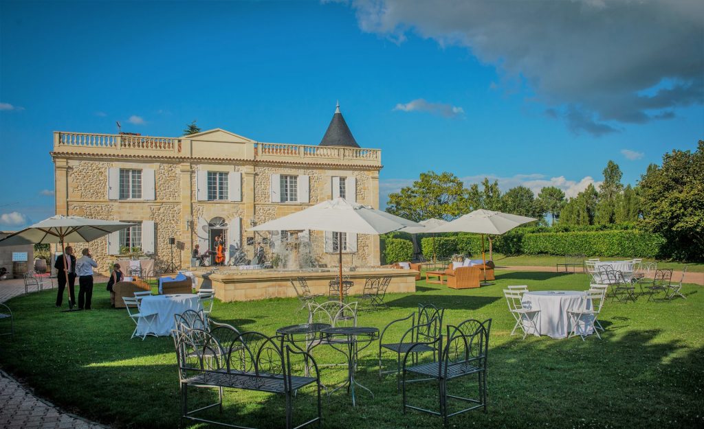 Pelouse du château Lafitte aménagée de tables et de parasols blancs devant la façade et sa fontaine