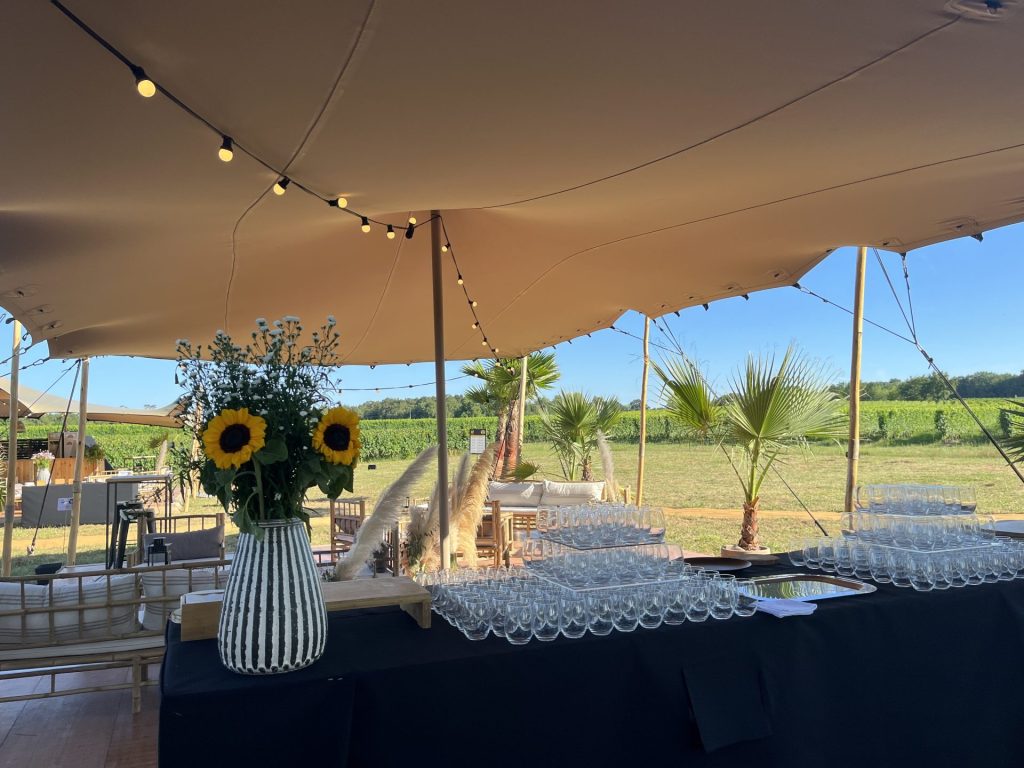 Table de service sous une tente face aux vignes, avec verres alignés et bouquet de tournesols, pendant le séminaire organisé par Weevup au château Lafitte
