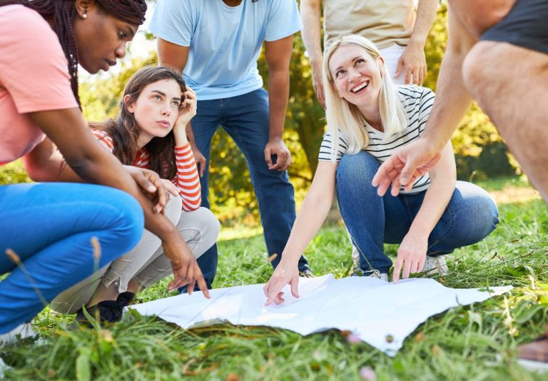 Collègues réunis dans l’herbe autour d’une carte dépliée lors d’une chasse au trésor en team building