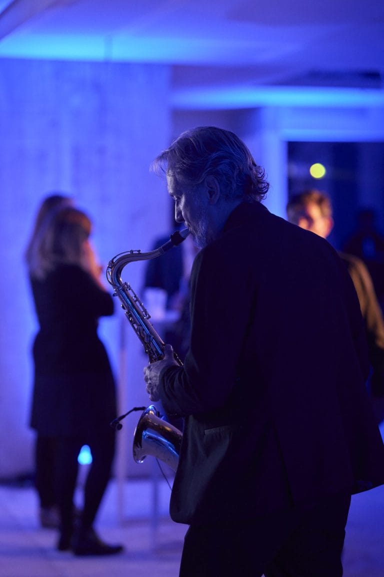 Saxophoniste jouant sous des lumières bleues, invités en arrière-plan, pendant la soirée Delpha organisée par Weevup sur un chantier encore en activité