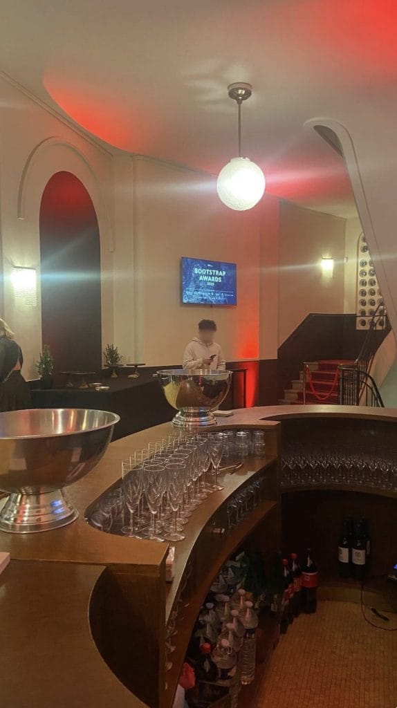 Bar du cocktail dînatoire sous un éclairage rouge, escalier à tapis rouge au fond, événement du Club Boostrap organisé par Weevup dans un théâtre historique