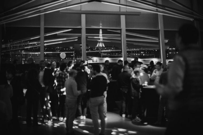 Participants réunis en soirée devant de grandes baies vitrées, tour Eiffel illuminée au loin, pendant la convention annuelle de 3DS Outscale