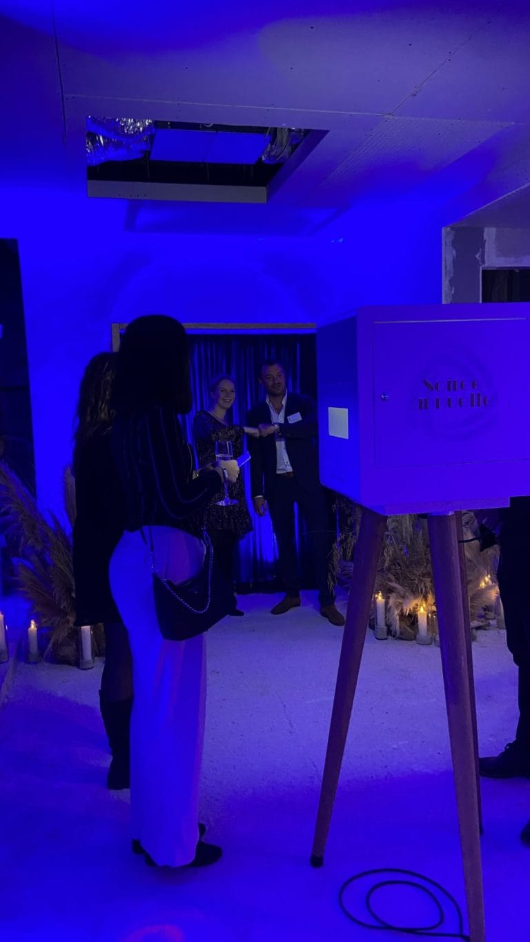 Invités de la soirée Delpha sous des lumières bleues, près d’une borne en bois sur trépied et de bougies, sur le chantier où Weevup a organisé la réception