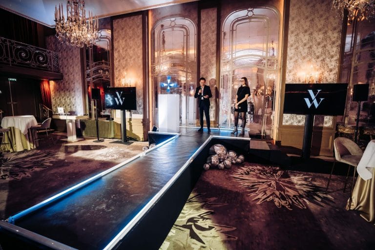 Podium éclairé de bleu dans un salon à lustres et moulures, entre des écrans au logo de la marque, installé par Weevup pour la soirée de lancement Vanessa Wu