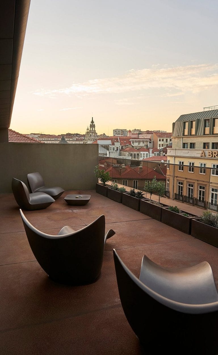 Terrasse d’hôtel aux fauteuils design, face aux toits de Porto au coucher du soleil