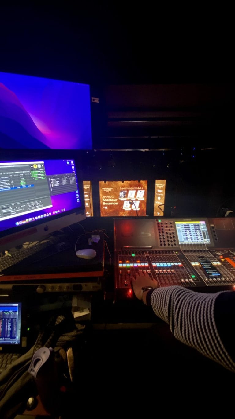 Technicien à la régie son et lumière, écrans allumés et scène au fond, pendant la soirée Club Boostrap