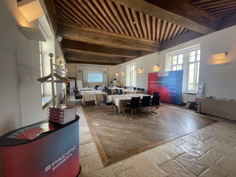 Salle de séminaire aux poutres apparentes du Château de Pizay, avec ses tables nappées de blanc, son écran et le kakémono Pacific, préparée pour le séminaire de Pacific et Général