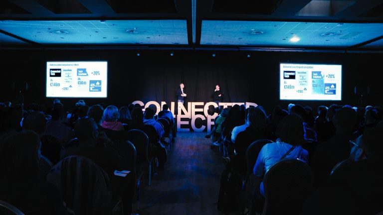Deux intervenants sur scène devant le public de la plénière KPMG Connected Tech 2024, entre deux écrans géants