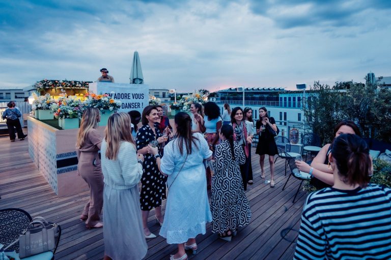 Invités de la cocktail party Dior réunis sur un rooftop au plancher de bois, à la tombée du jour