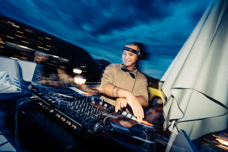 DJ aux platines à la nuit tombante, près d’un parasol, pendant la cocktail party d’été de Dior organisée par Weevup sur un rooftop