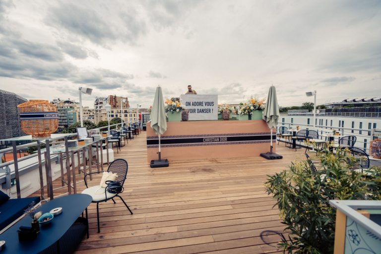 Rooftop au plancher de bois avec parasols fermés et salons de jardin, préparé pour la cocktail party Dior