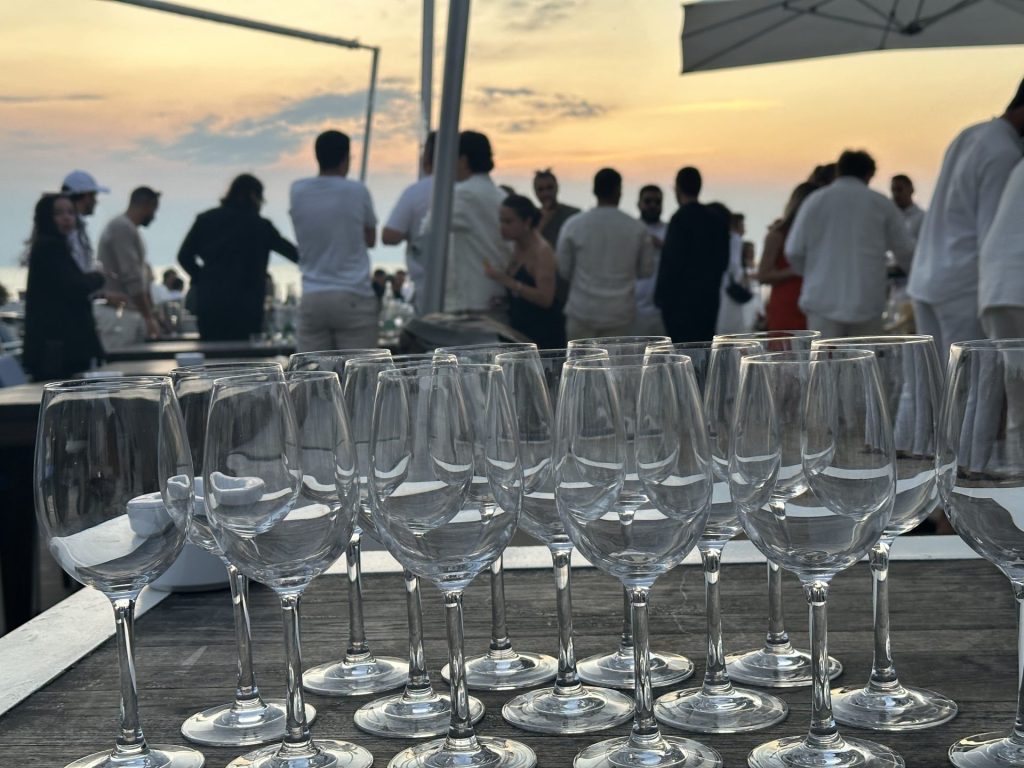 Coucher de soleil sur la mer, verres alignés au premier plan et participants en terrasse, pendant le séminaire annuel de MYM organisé par Weevup