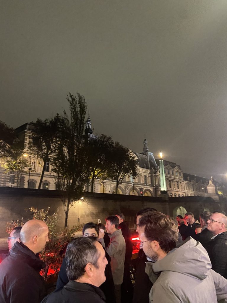 Invités de la soirée post-salon Hanwha sur le pont de la péniche River’s King, devant les façades illuminées des quais de Seine, à Paris
