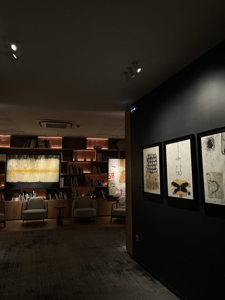 Couloir aux murs sombres orné de dessins encadrés, ouvrant sur un salon avec bibliothèque et fauteuils, photographié pendant le séminaire Swiss Life à Reims