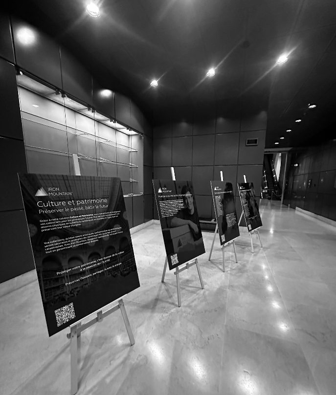 Panneaux Iron Mountain « Culture et patrimoine », avec QR codes, posés sur des chevalets le long d’un couloir, pour le dîner au Louvre (photo en noir et blanc)