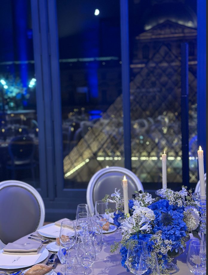 Table du dîner Iron Mountain dressée de fleurs bleues et blanches face à la pyramide du Louvre, scénographie Weevup