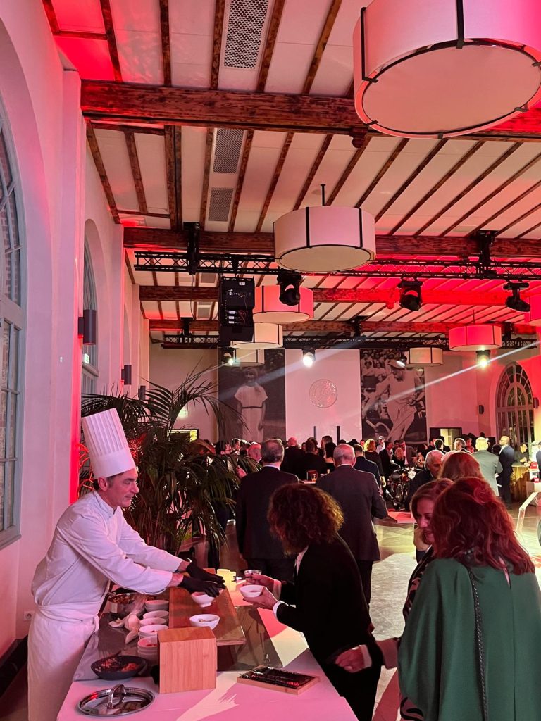 Chef en toque servant les invités à un stand culinaire, sous un éclairage rouge, pendant la soirée de passation de Cofinas organisée par Weevup à l’Orangerie d’Auteuil