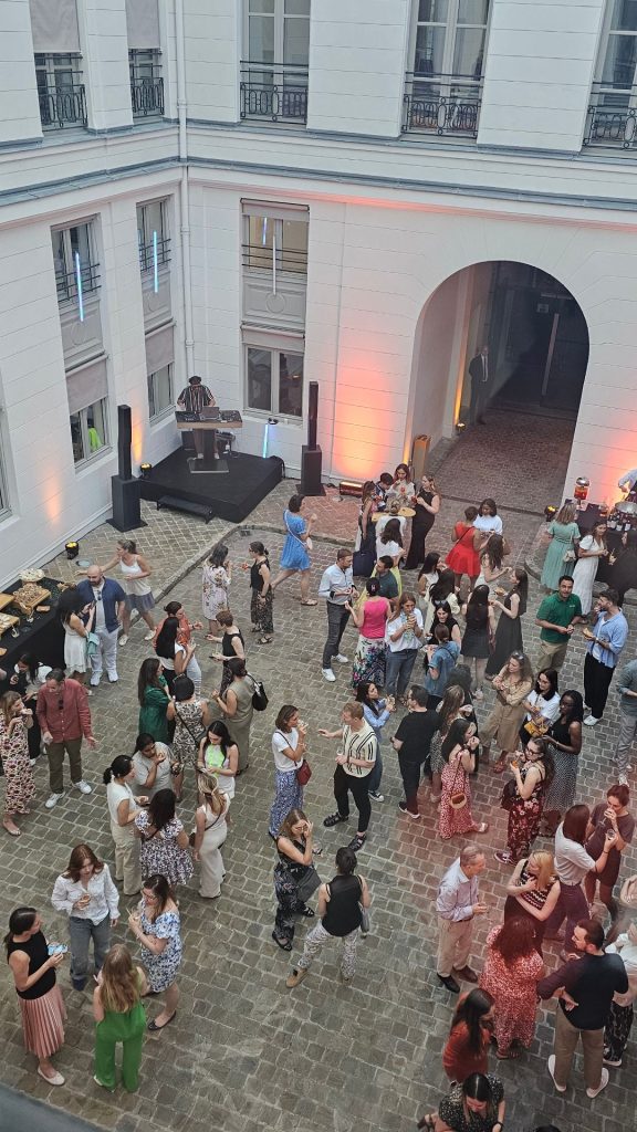 Vue plongeante sur la Summer Party Coty 2025 dans une cour intérieure : DJ, convives debout, ambiance décontractée et festive.