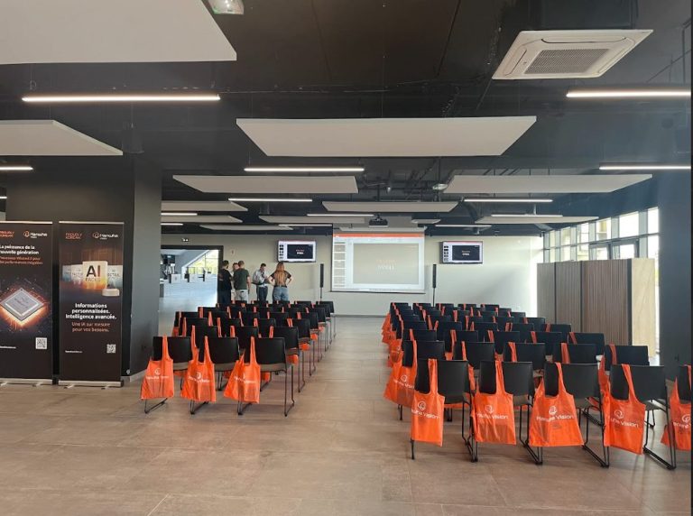 Salle de conférence lumineuse aux chaises alignées, garnies de sacs orange Hanwha Vision, avant une présentation du roadshow Hanwha à Agen