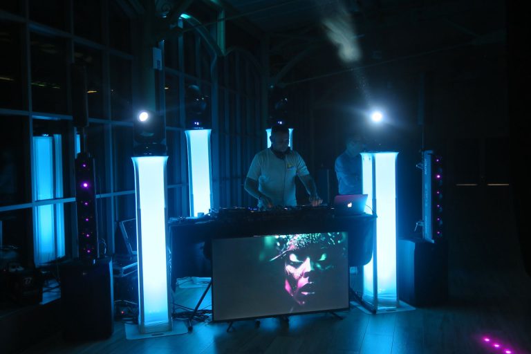 DJ aux platines entre des colonnes lumineuses bleues, en fin de soirée annuelle d’IGAM