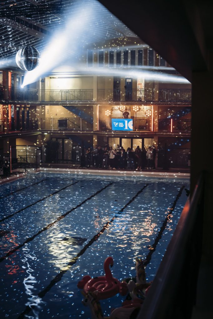 Boule à facettes et faisceaux lumineux au-dessus du bassin du Molitor, invités au bord de l’eau, pendant la pool party des 10 ans de Weevup