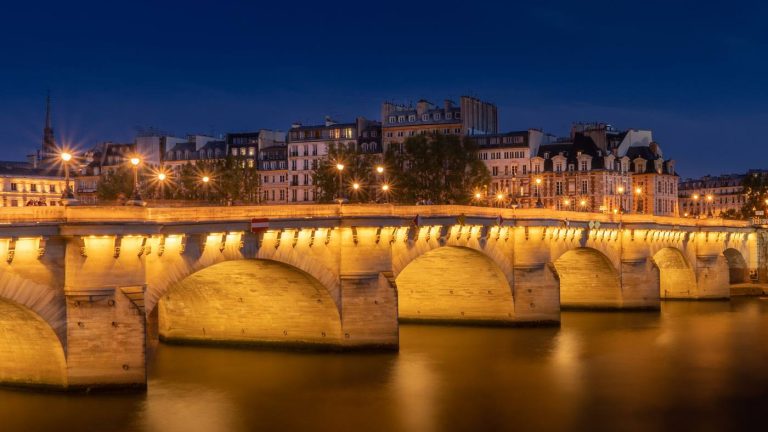 Le Pont-Neuf illuminé se reflète dans la Seine, à Paris, à la tombée de la nuit
