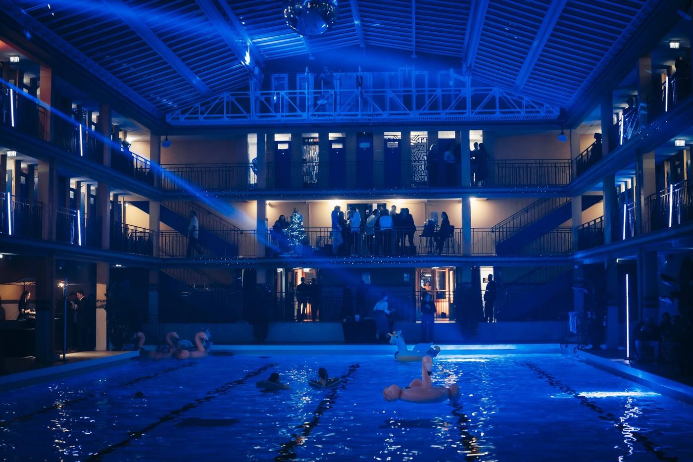 Piscine du Molitor éclairée en bleu, avec des bouées sur le bassin et des invités aux balcons des coursives, pendant la soirée des 10 ans de Weevup