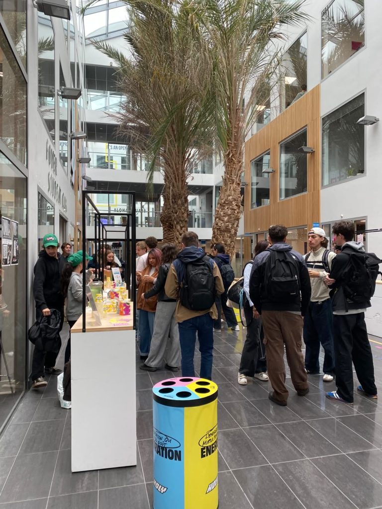 Stand de dégustation Holy installé dans le hall d’une école, avec une poubelle à gobelets Hydration et Energy aux couleurs de la marque
