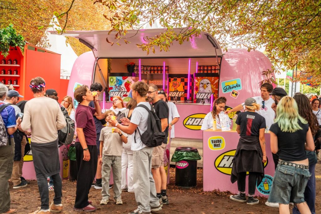 Espace Holy à Rock en Seine : caravane rose, comptoirs « Taste me ! », poubelle Holy et festivaliers, gobelet en main
