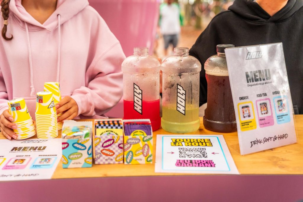 Carafes Holy rouge, verte et thé glacé, menu « Dégustations gratuites » et QR code du jeu « Tourne la roue » sur le comptoir