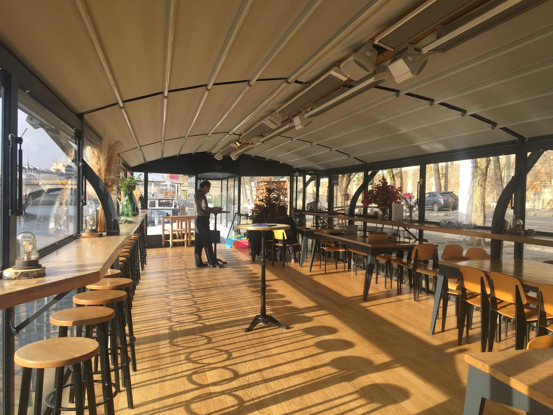 Pont couvert d'une péniche privatisée par Weevup en bord de Seine, avec comptoir en bois, tabourets et tables baignés de soleil