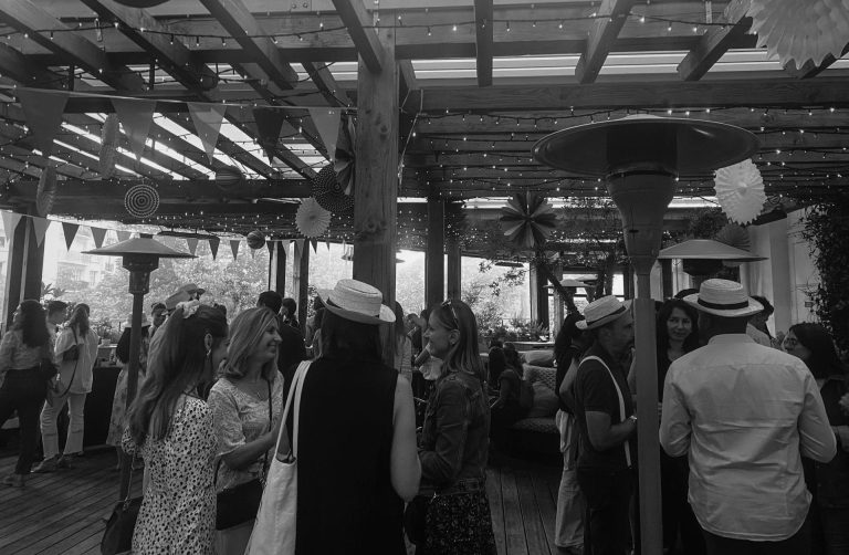 Invités de la soirée de rentrée Coty réunis sous la pergola de la Brasserie Auteuil, décorée de fanions et de guirlandes lumineuses (photo en noir et blanc)