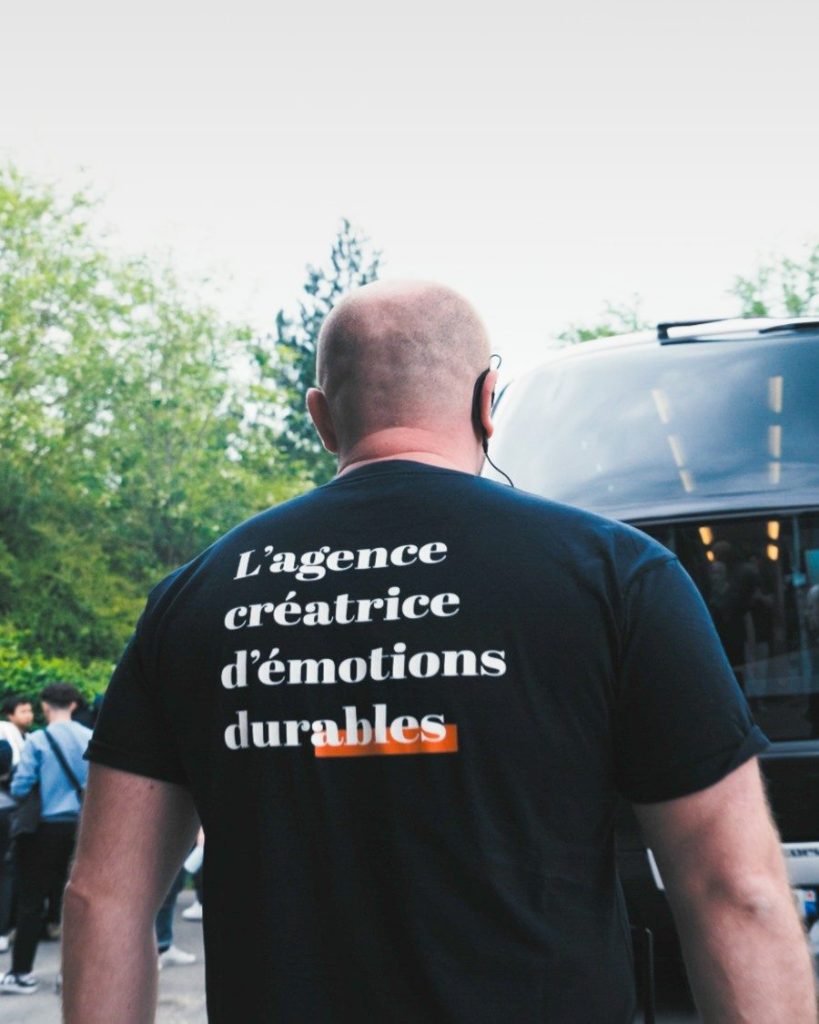 Membre de l’équipe Weevup de dos, tee-shirt « L’agence créatrice d’émotions durables », à l’accueil des participants d’un séminaire d’entreprise
