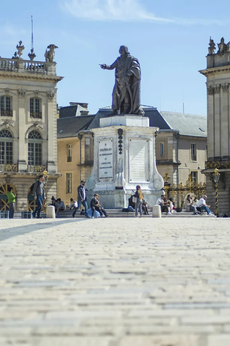 La statue de Stanislas sur son piédestal, entre les façades de la place Stanislas, à Nancy, sous un ciel bleu