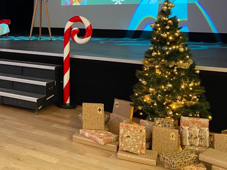 Sapin aux boules dorées, cadeaux emballés et sucre d’orge géant au pied de la scène, pour le Noël solidaire de LEGO et Dons Solidaires