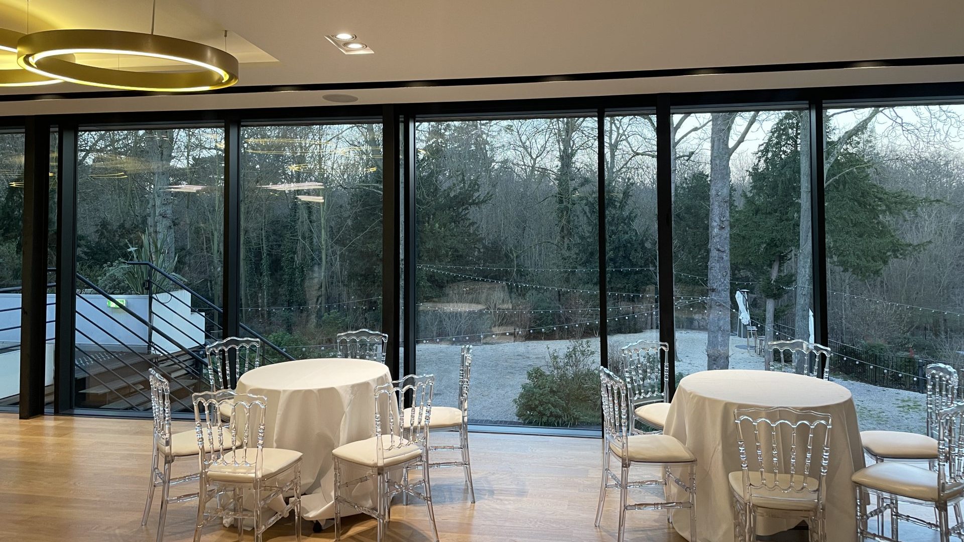 Tables rondes nappées de blanc et chaises transparentes dans un pavillon vitré ouvert sur un jardin arboré, au Pavillon Royal, pour la convention annuelle 3DS Outscale organisée par Weevup